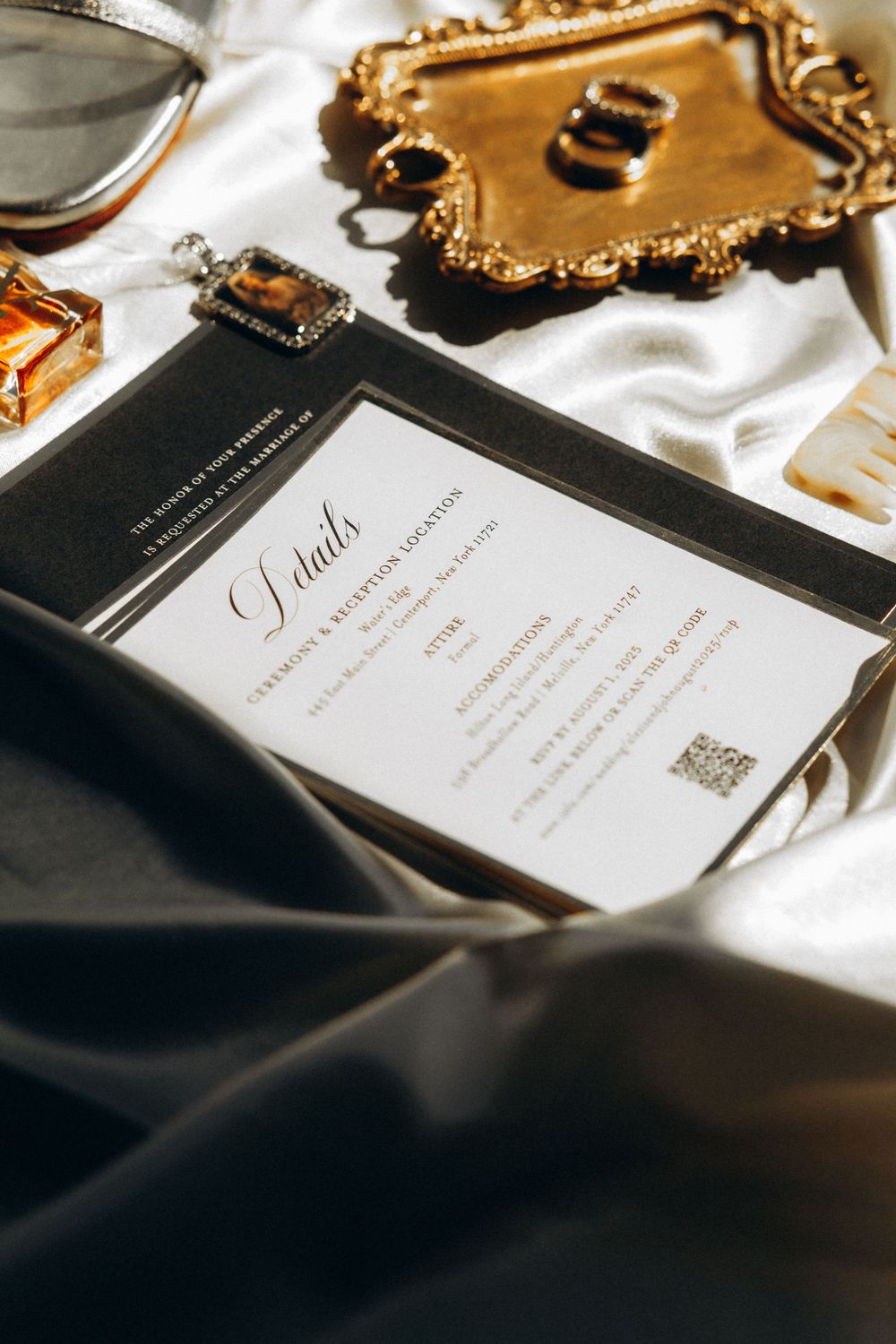 Elegant wedding invitation cards with gold accents and calligraphy text laid out on white fabric in soft lighting.