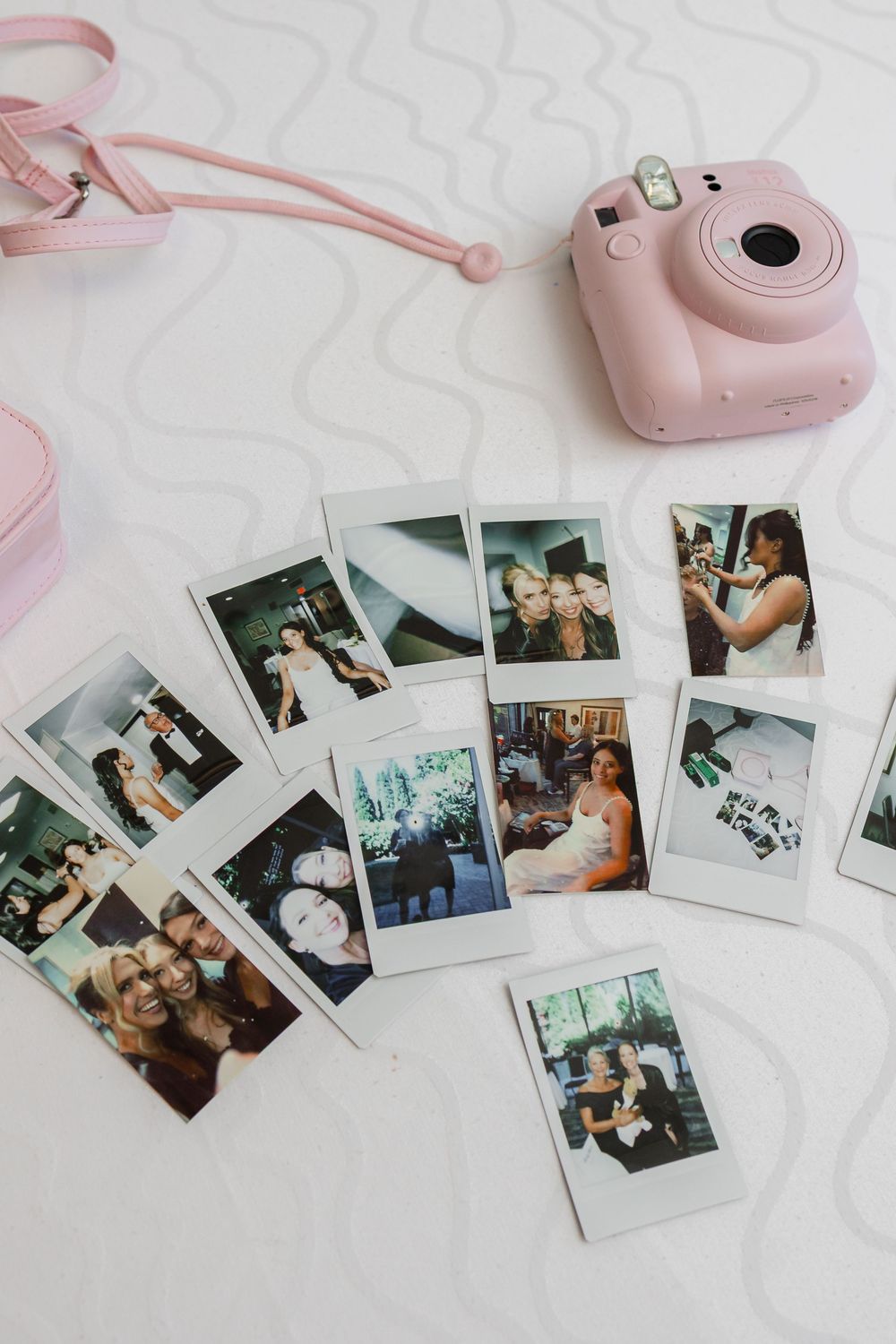 Pink Instax camera with scattered instant photo prints laid out on white marble surface.