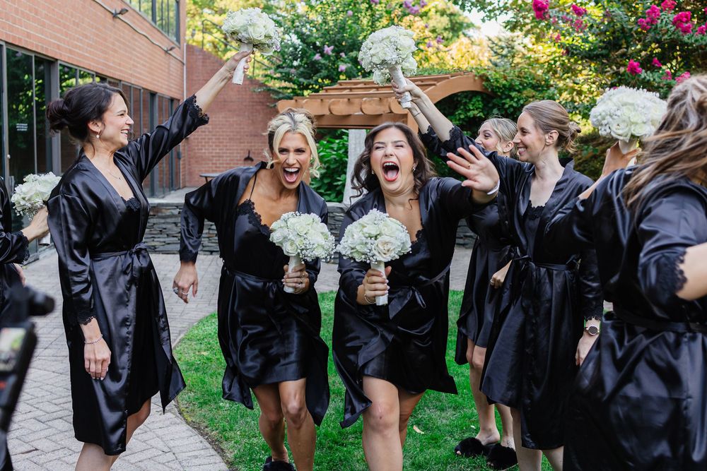 A group of graduates in black gowns celebrate by tossing their caps in the air during an outdoor graduation ceremony.