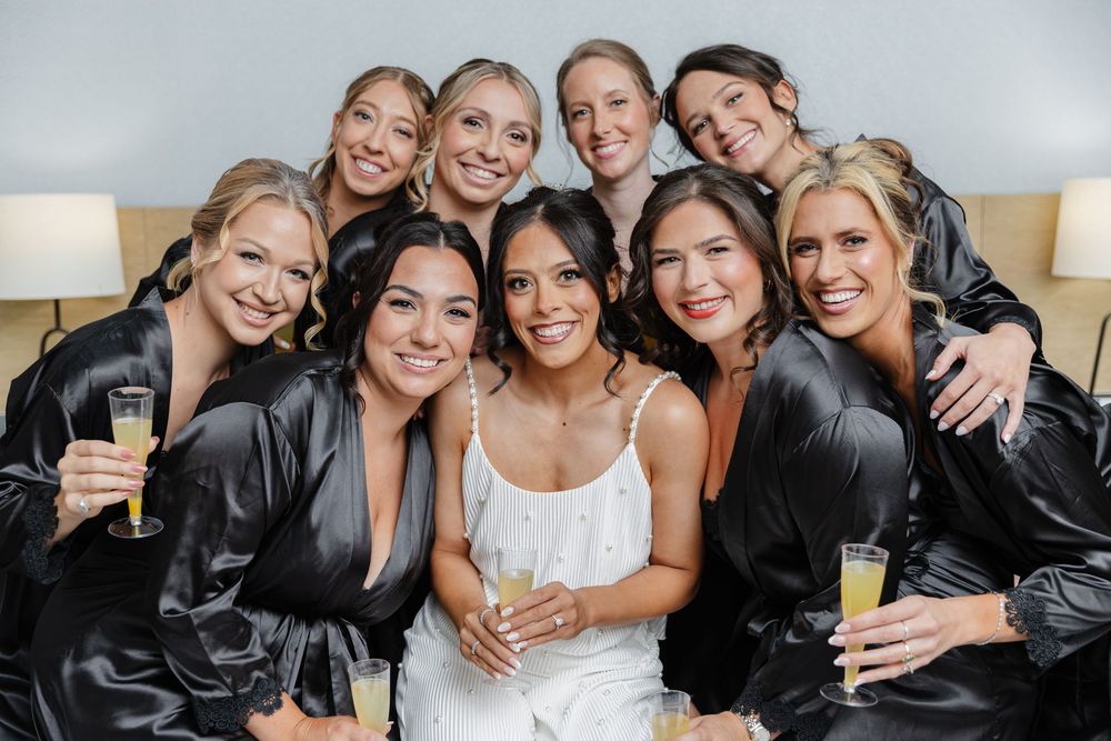 A group of people in formal attire pose together for wedding photos, smiling and embracing.