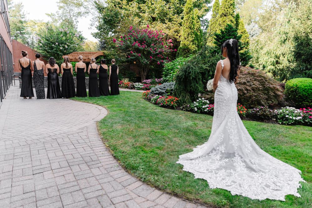 A bride in a flowing white lace gown with a long train poses in a lush garden setting during a wedding photoshoot.