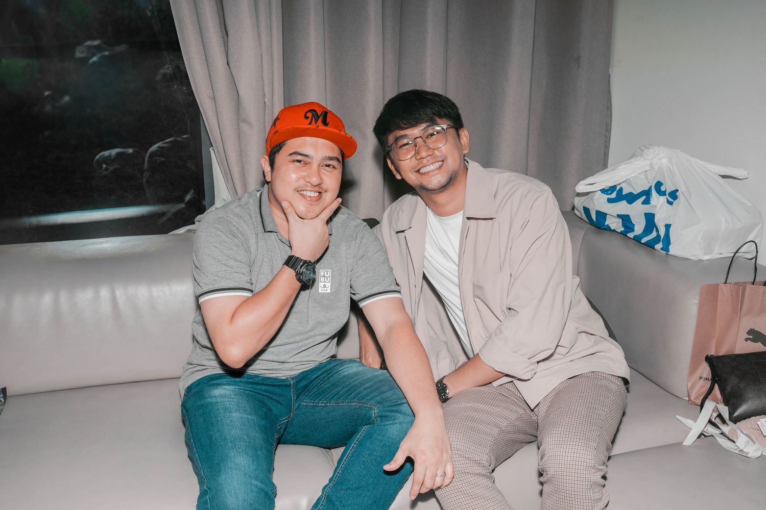 Two friends sit together on a white couch during a casual gathering.