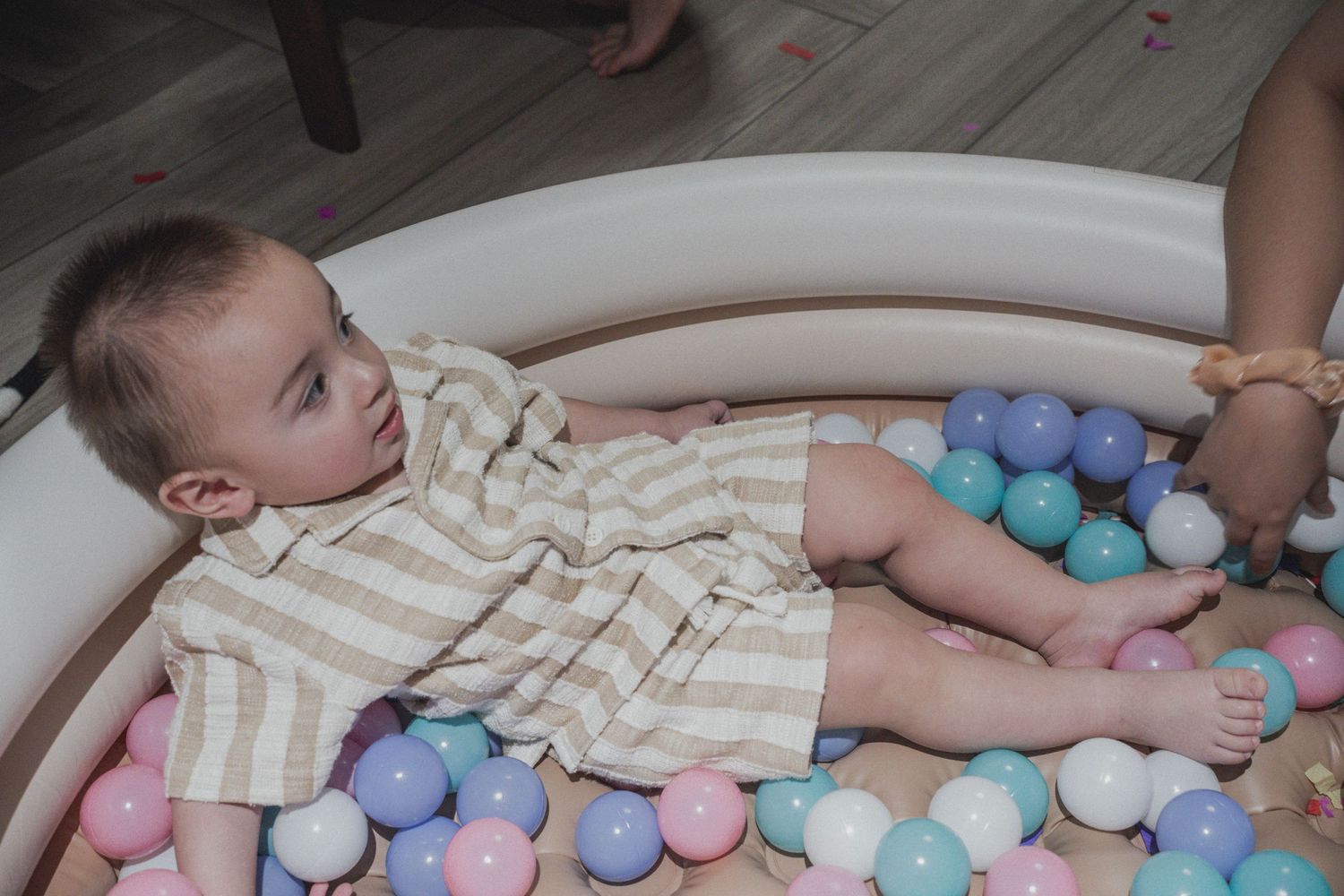 Baby lying in ball pit filled with pastel colored balls.