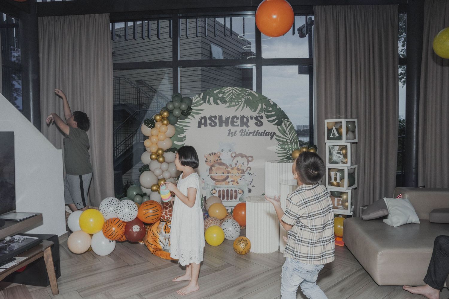 A party space decorated with balloons and floral arrangements against white curtains.