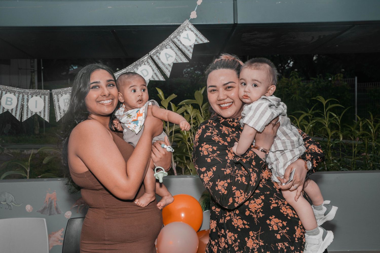 Two women in festive attire celebrate at a tropical-themed birthday party with balloons.
