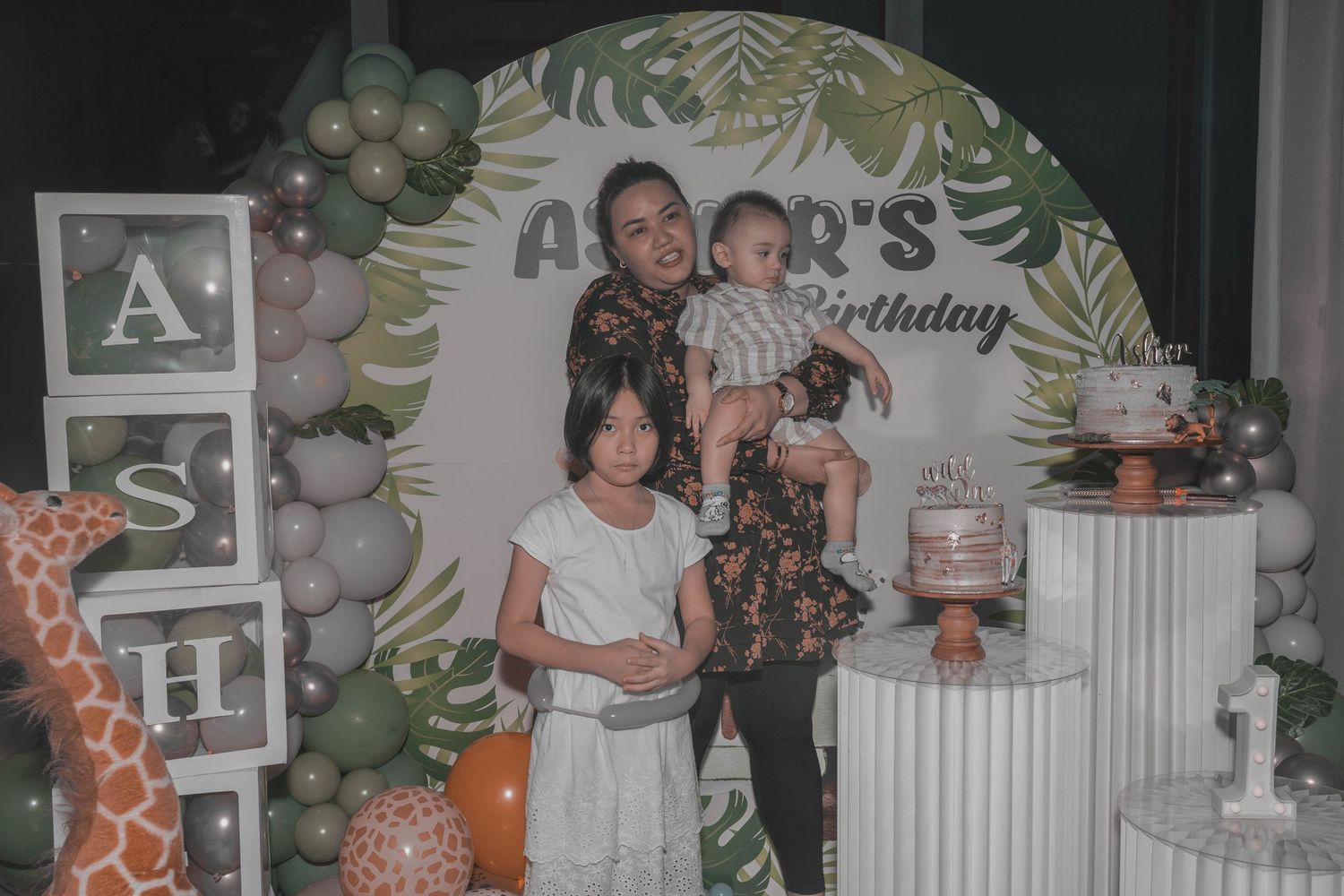A tropical-themed first birthday party setup with balloon decorations and a 'Wild One' theme featuring palm leaf designs.