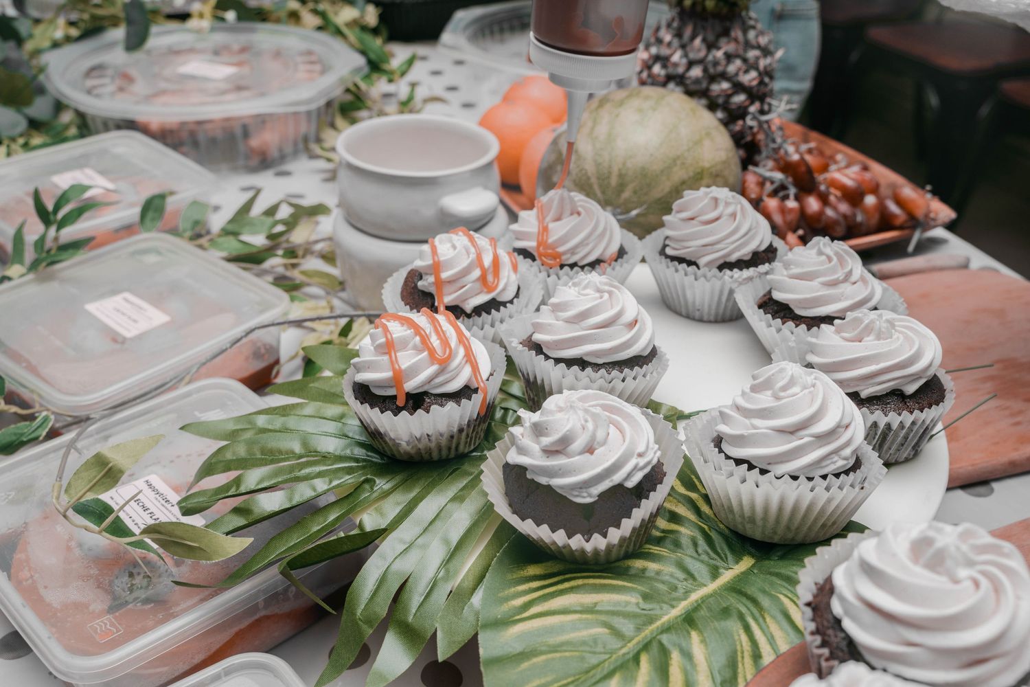 Decorated cupcakes with white frosting displayed on tropical leaves at a party.