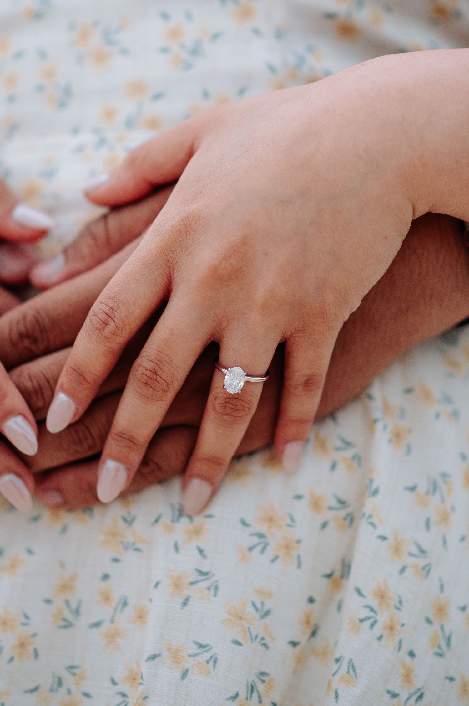 Engagement ring detail shot with hands on floral patterned fabric.
