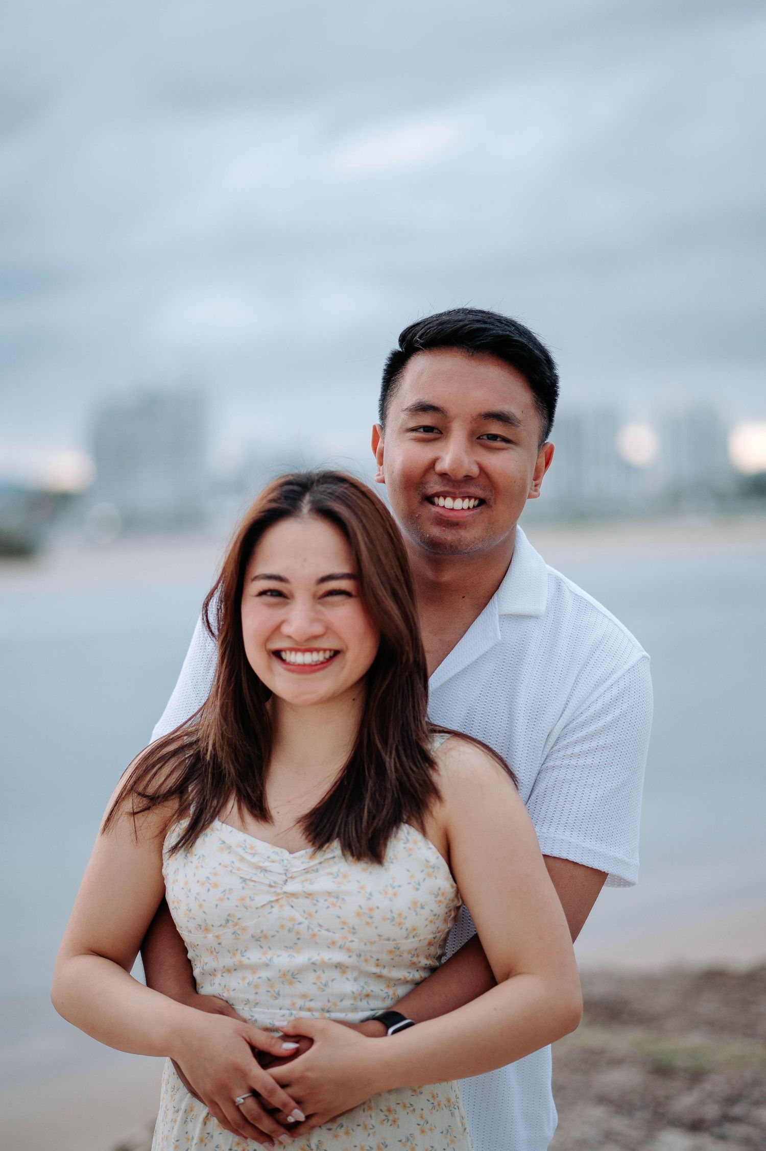 A loving couple embraces at the beach during golden hour with cloudy skies in the background.