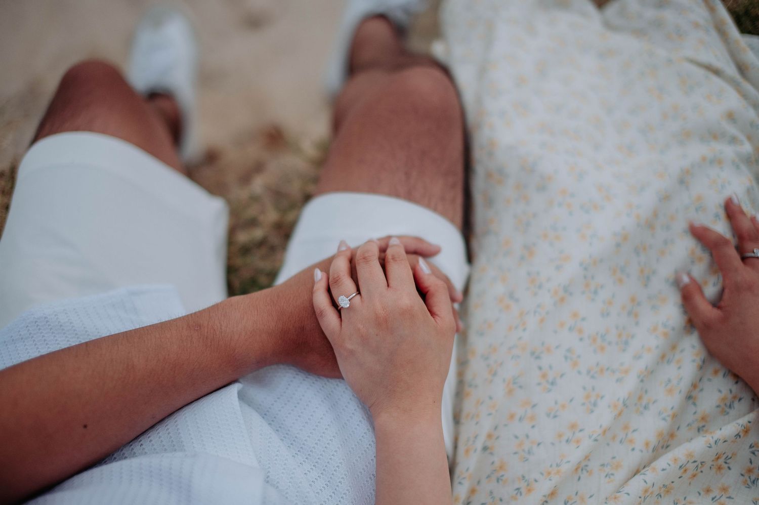 Close-up shot of couple holding hands while sitting on the sand at the beach.