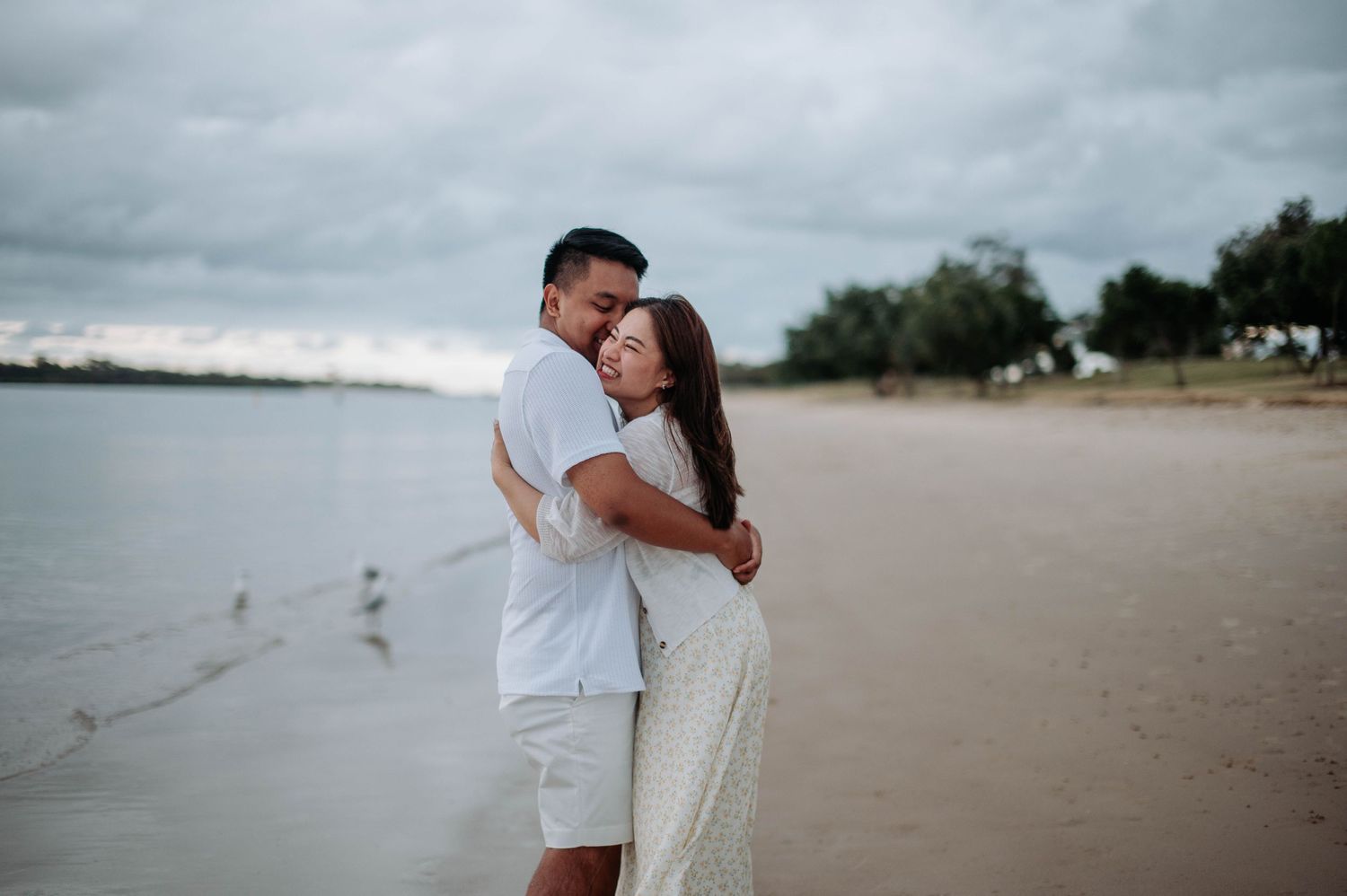 A couple shares an intimate embrace on a secluded beach during an overcast day.