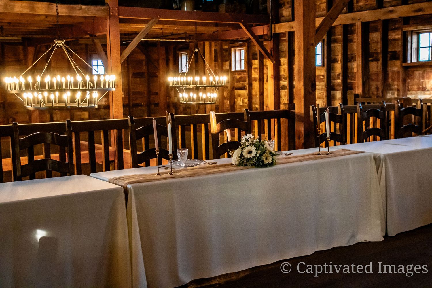 Elegant reception table setup with hanging chandeliers in a rustic wooden venue.