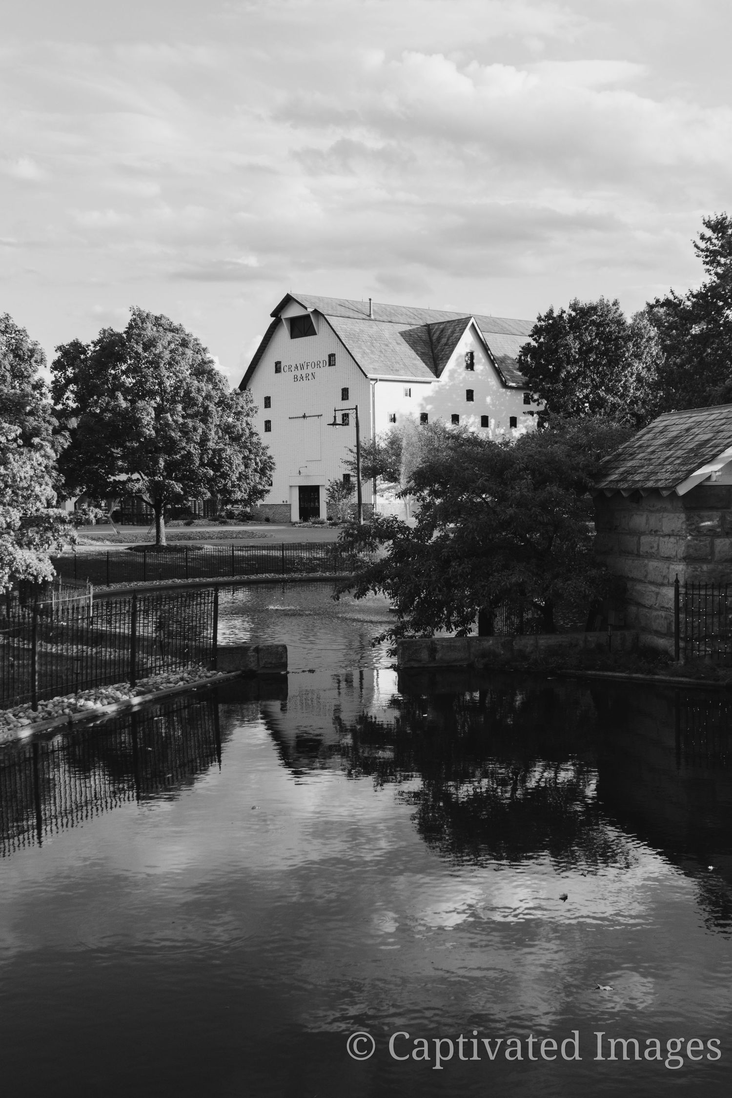 Black and white panoramic view of flooded buildings and trees along a waterway with reflections in still water.