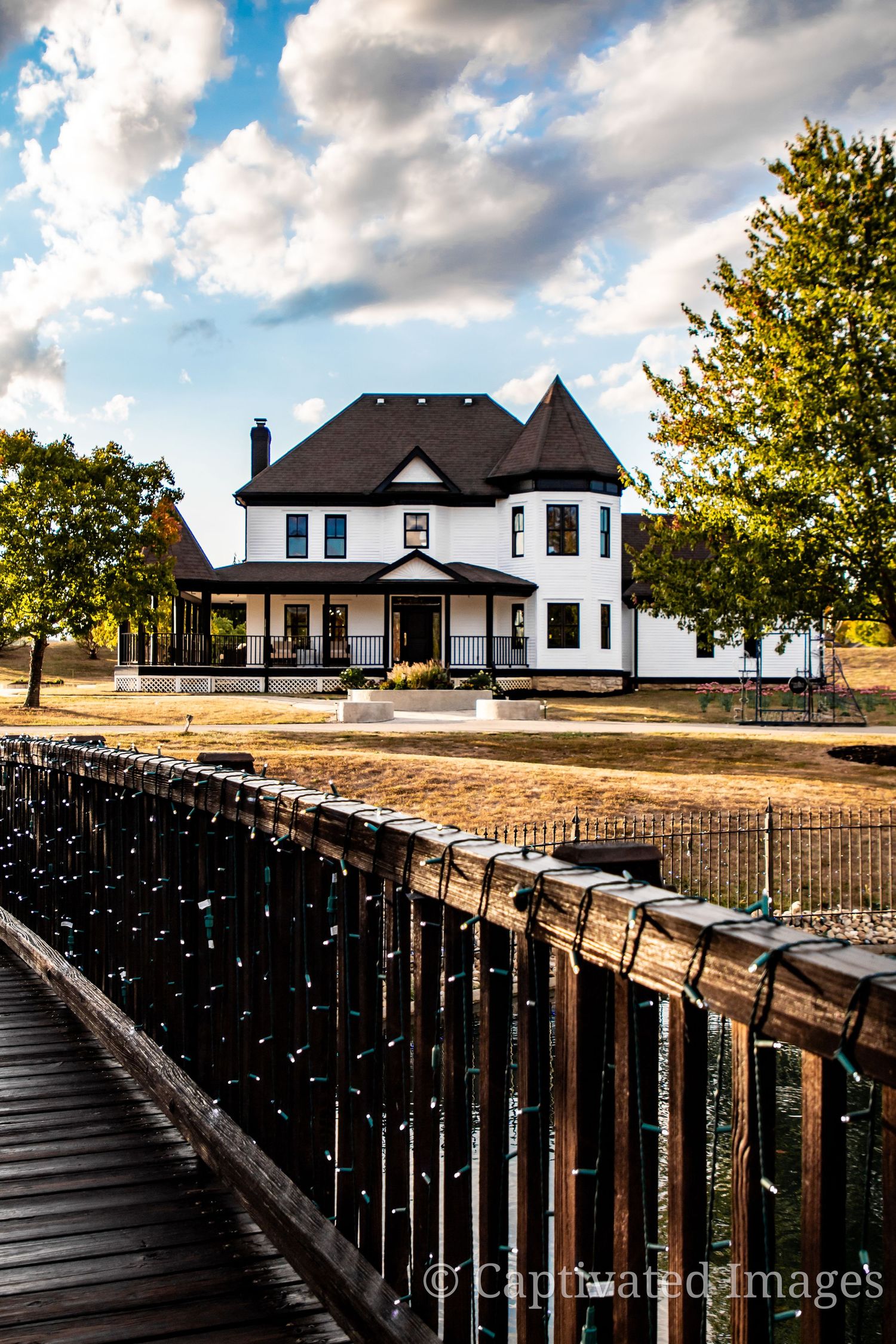 Victorian white house with wraparound porch viewed from curved iron bridge walkway.
