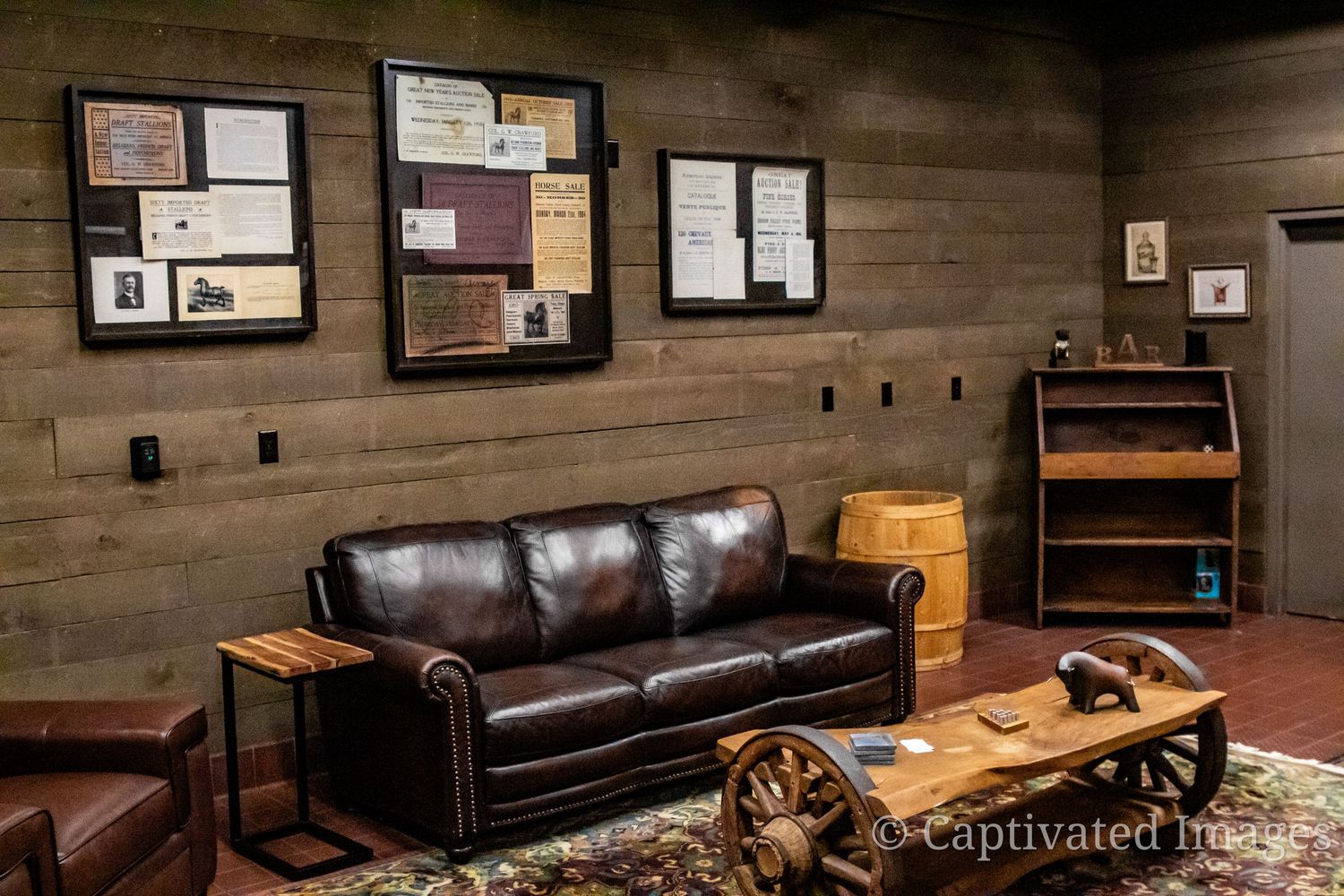 Modern rustic therapy office features dark leather couch, wood paneled walls, and framed artwork in a warm, inviting space.
