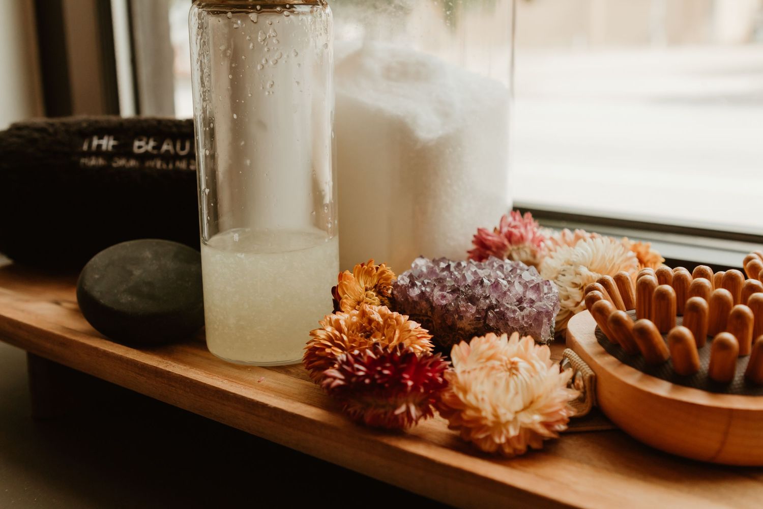 Dried flowers and glass jars sit on a wooden shelf near a window creating a rustic, minimalist display.
