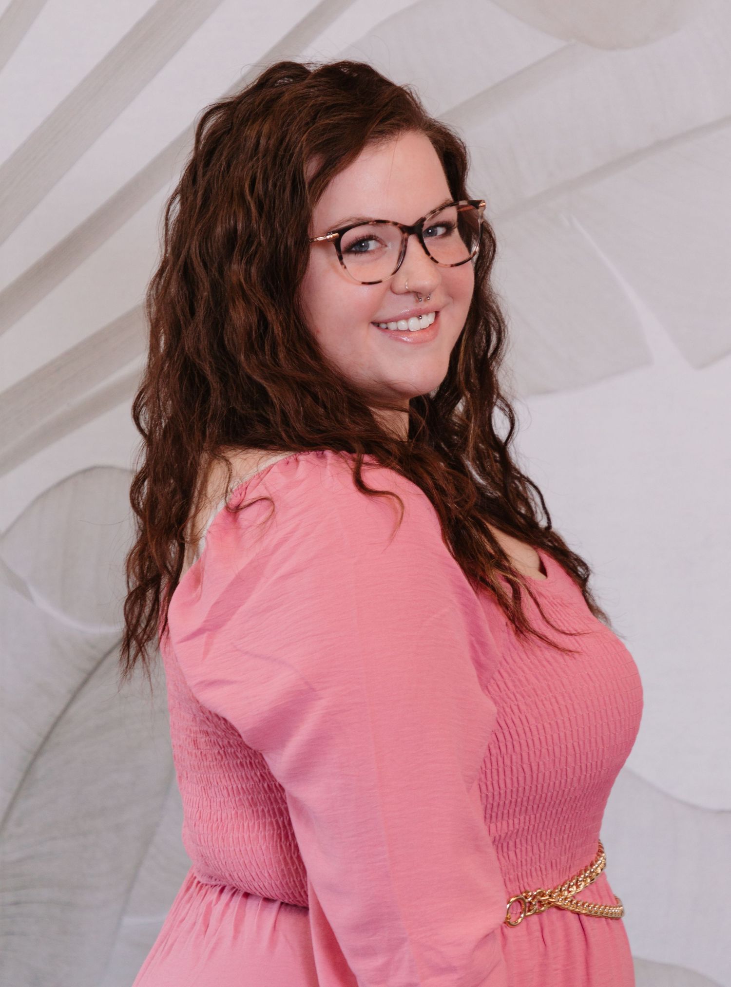 Professional portrait of a woman in a pink dress against a white textured background.