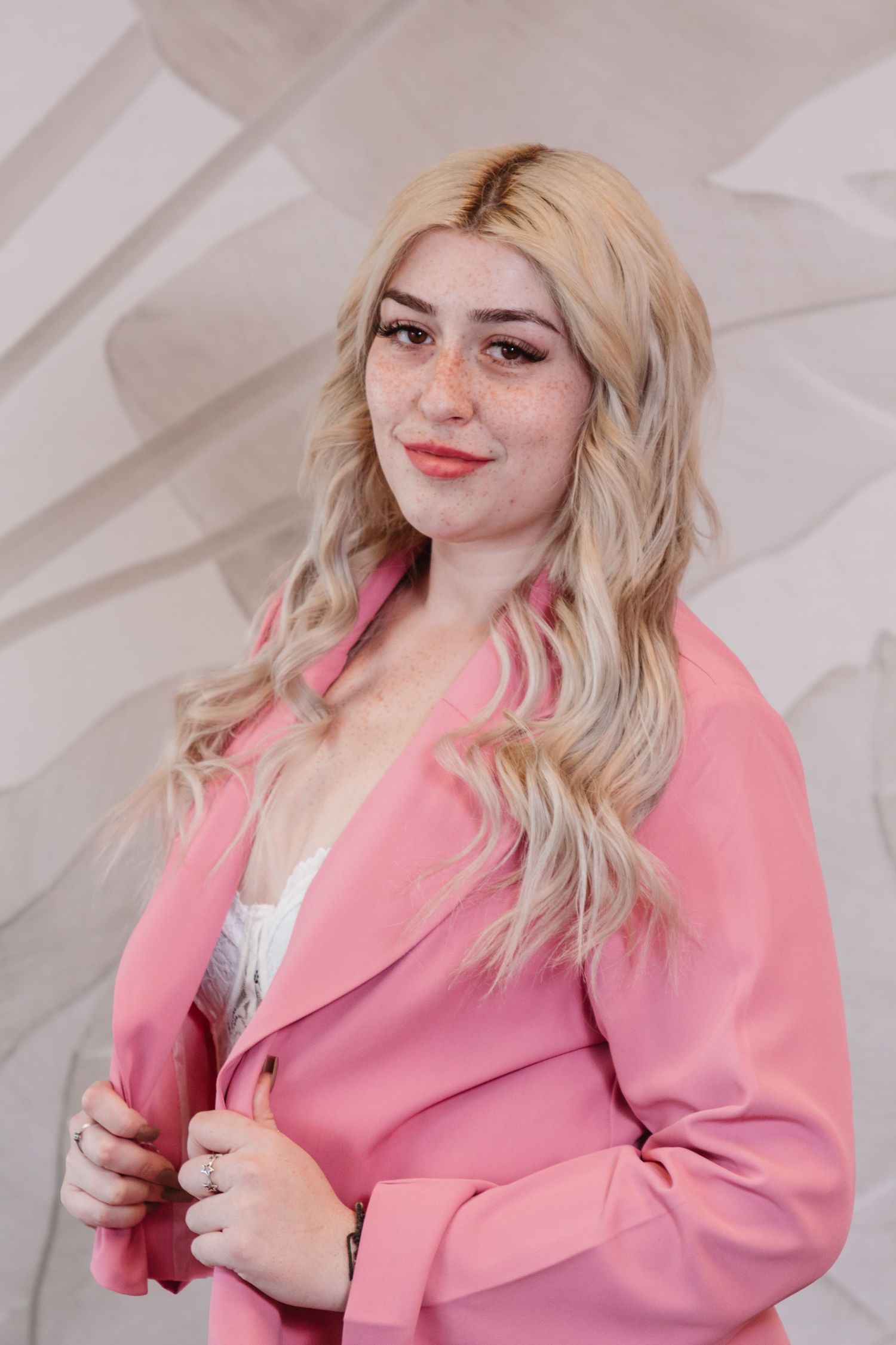 Studio portrait of a person in a pink blazer against a white geometric background.