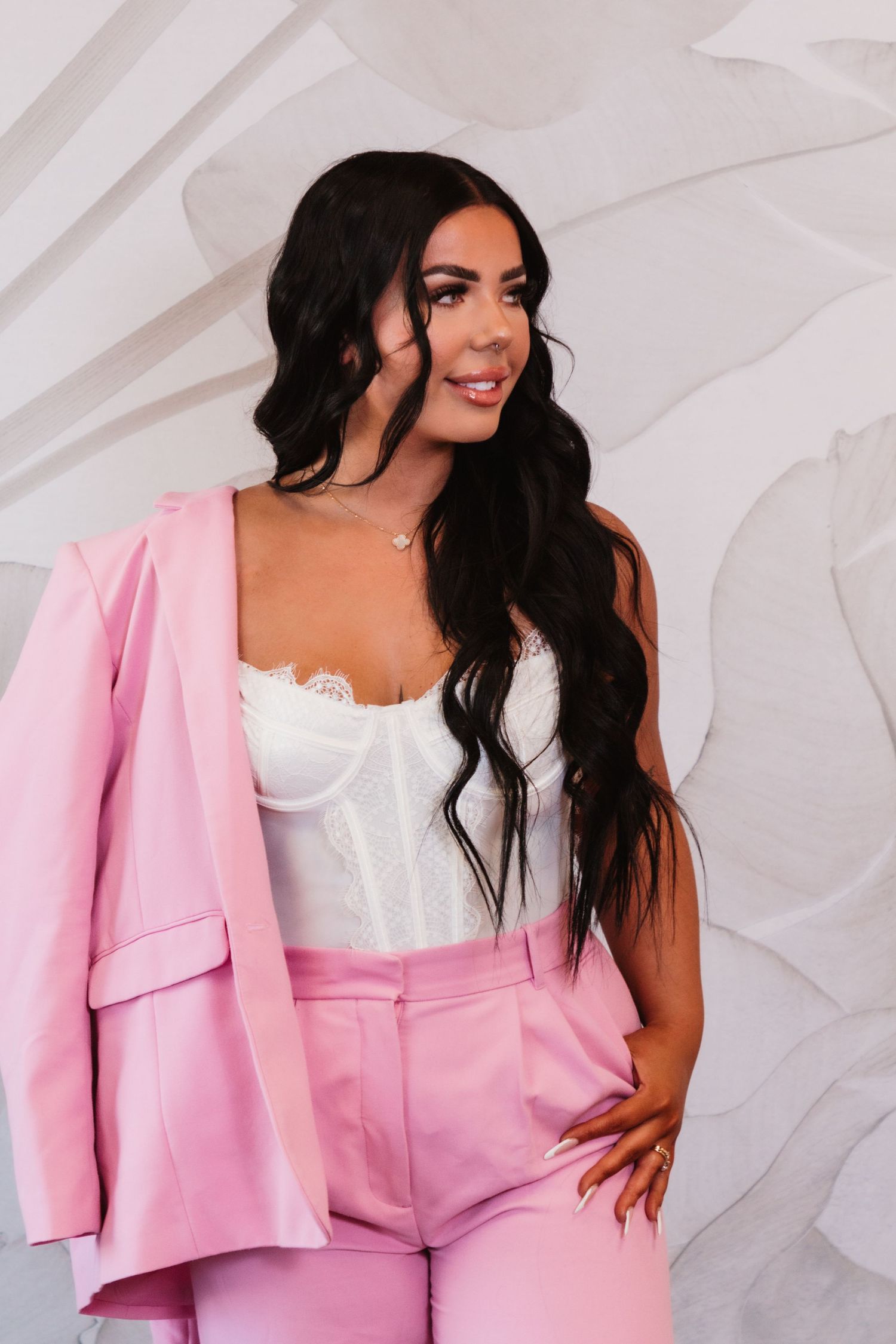 Fashionable portrait in a pink suit and white corset top against a textured white background.