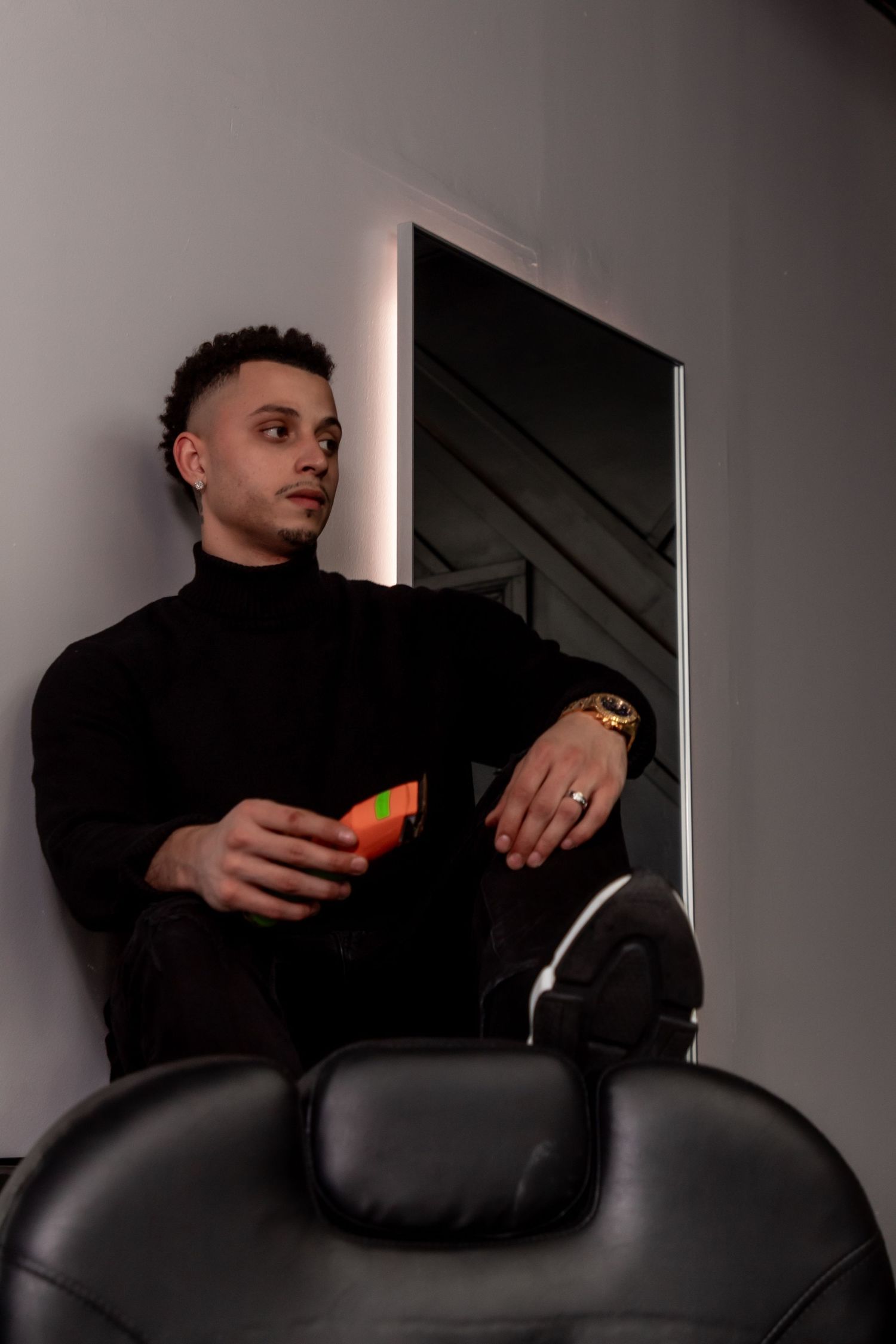 Person in black turtleneck sitting on a salon chair holding an orange object.