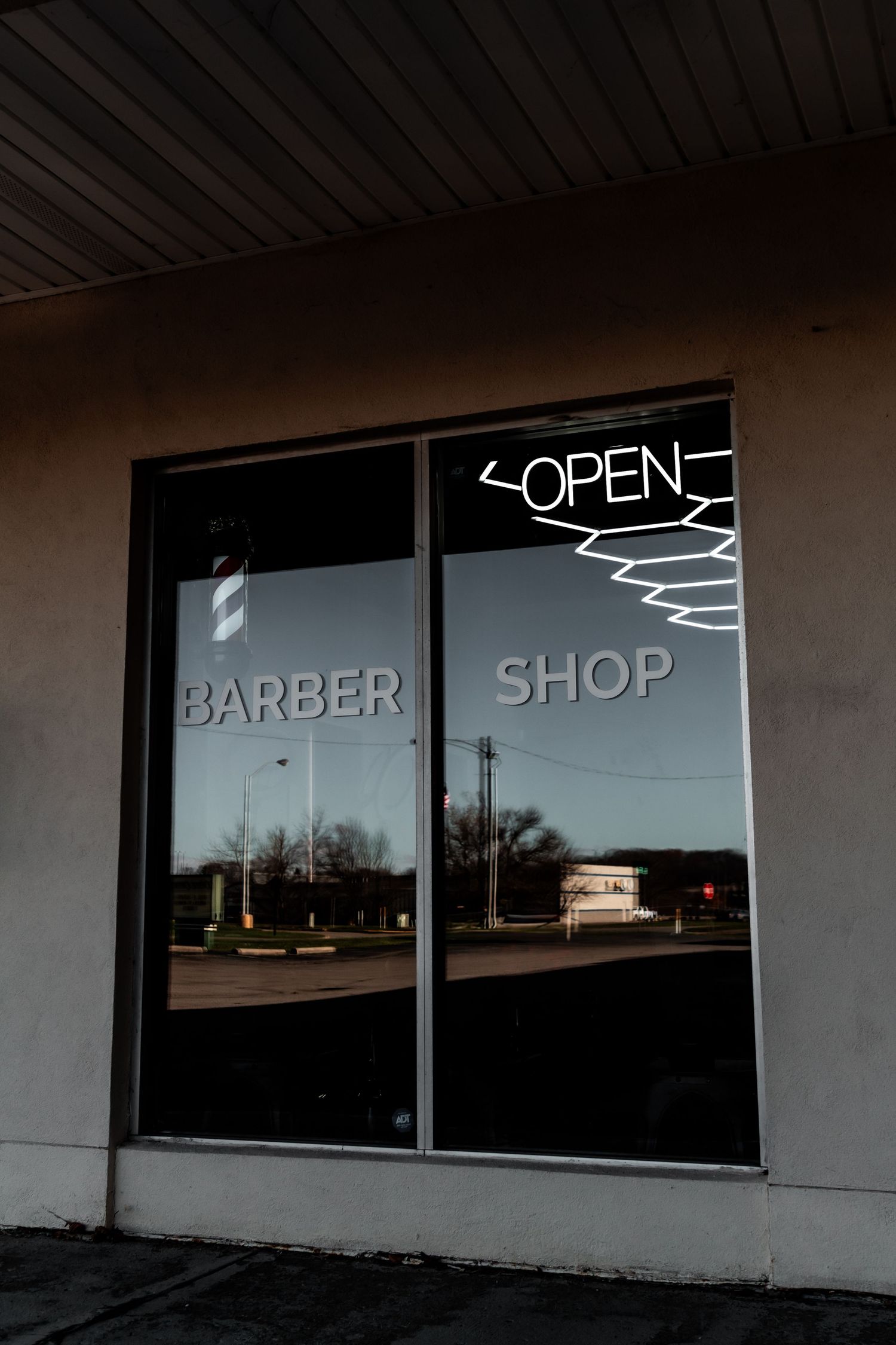 Exterior view of a barber shop storefront with an open neon sign in the window.
