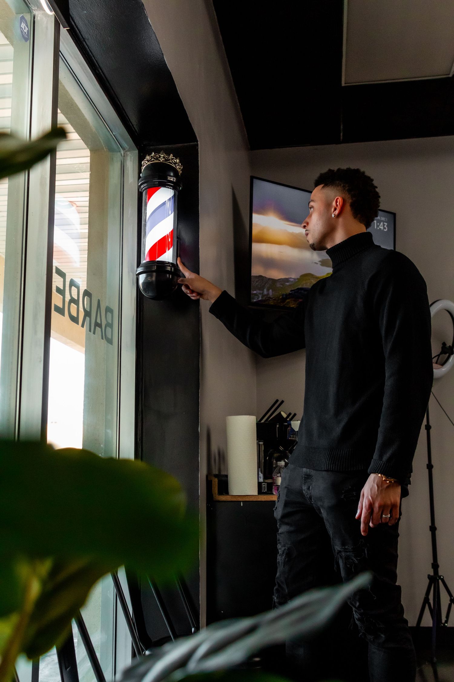 Person in black sweater touching a traditional barber pole in a modern salon setting.
