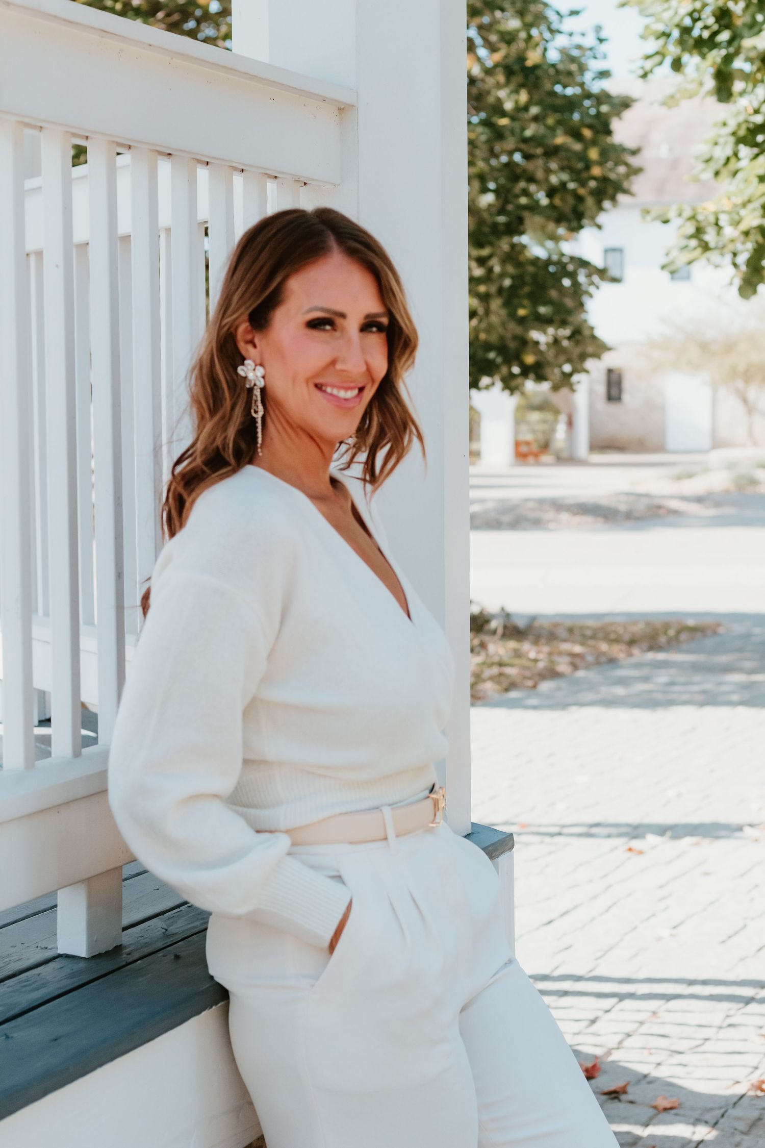 Elegant white long-sleeve dress pose against white porch railing.