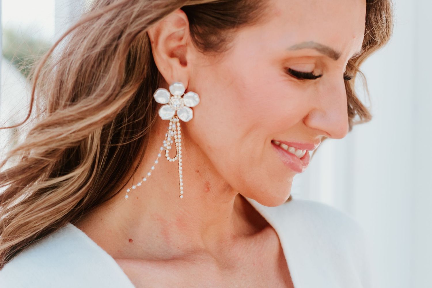Close up of ornate white floral earring and soft waves in hair.