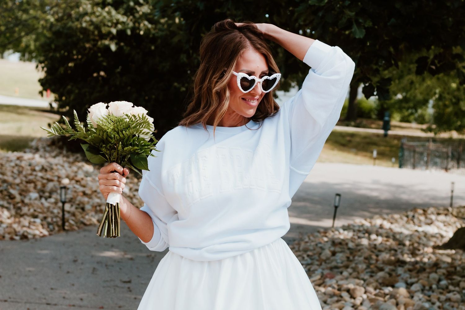 Playful pose in white sweater dress holding bouquet outdoors.