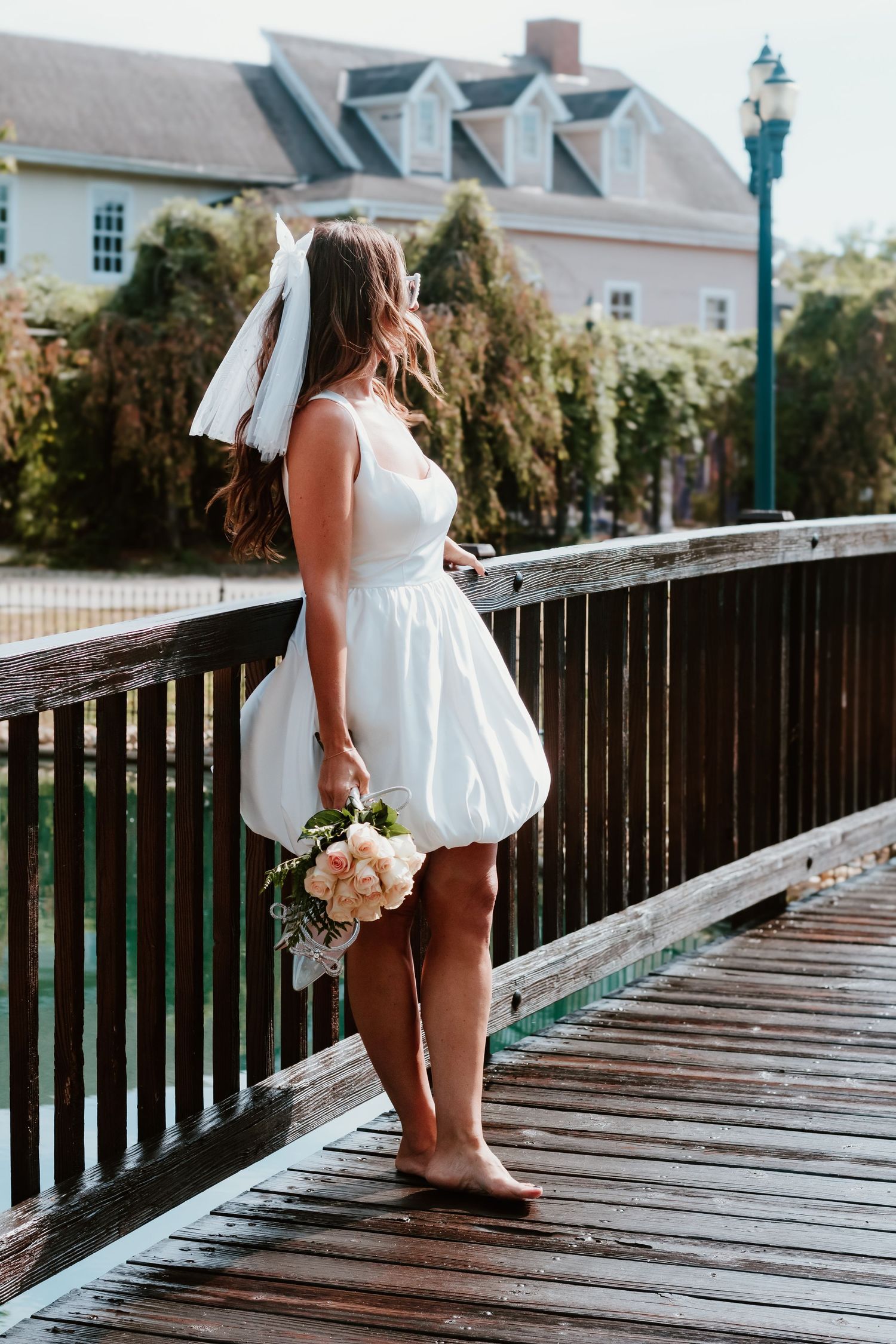 Bride in short white dress holding bouquet while standing on wooden bridge deck.