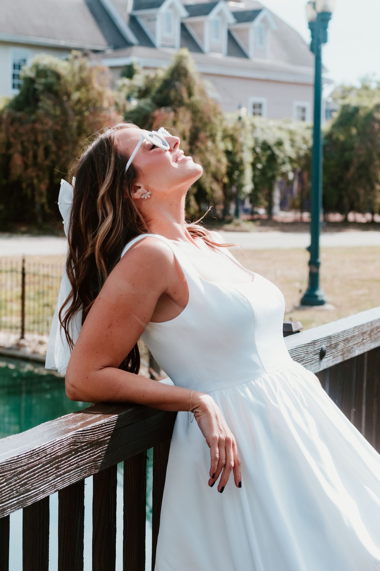Candid moment leaning against wooden railing in white dress outdoors.