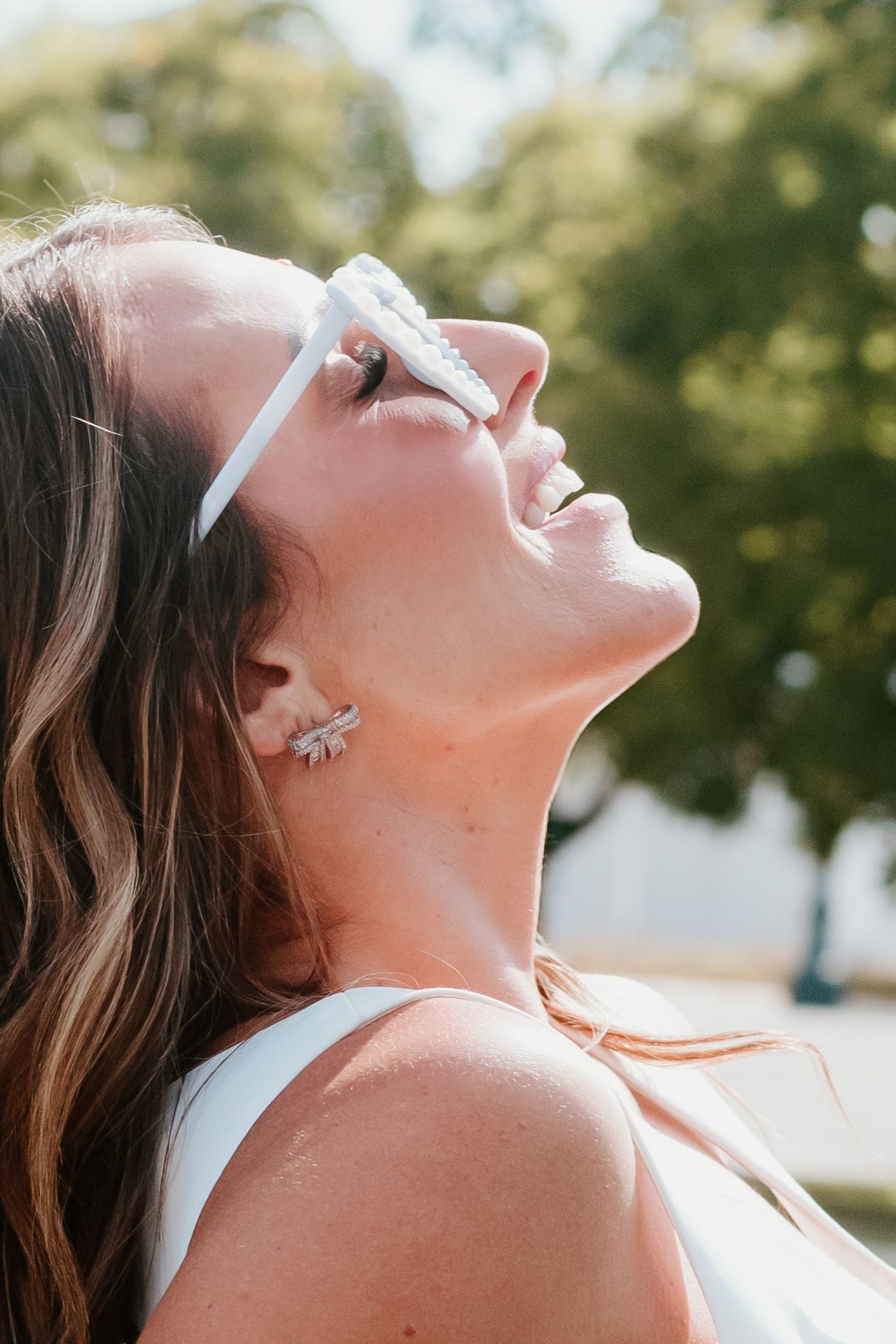Side profile portrait of carefree laughter with white sunglasses against sunny garden background.