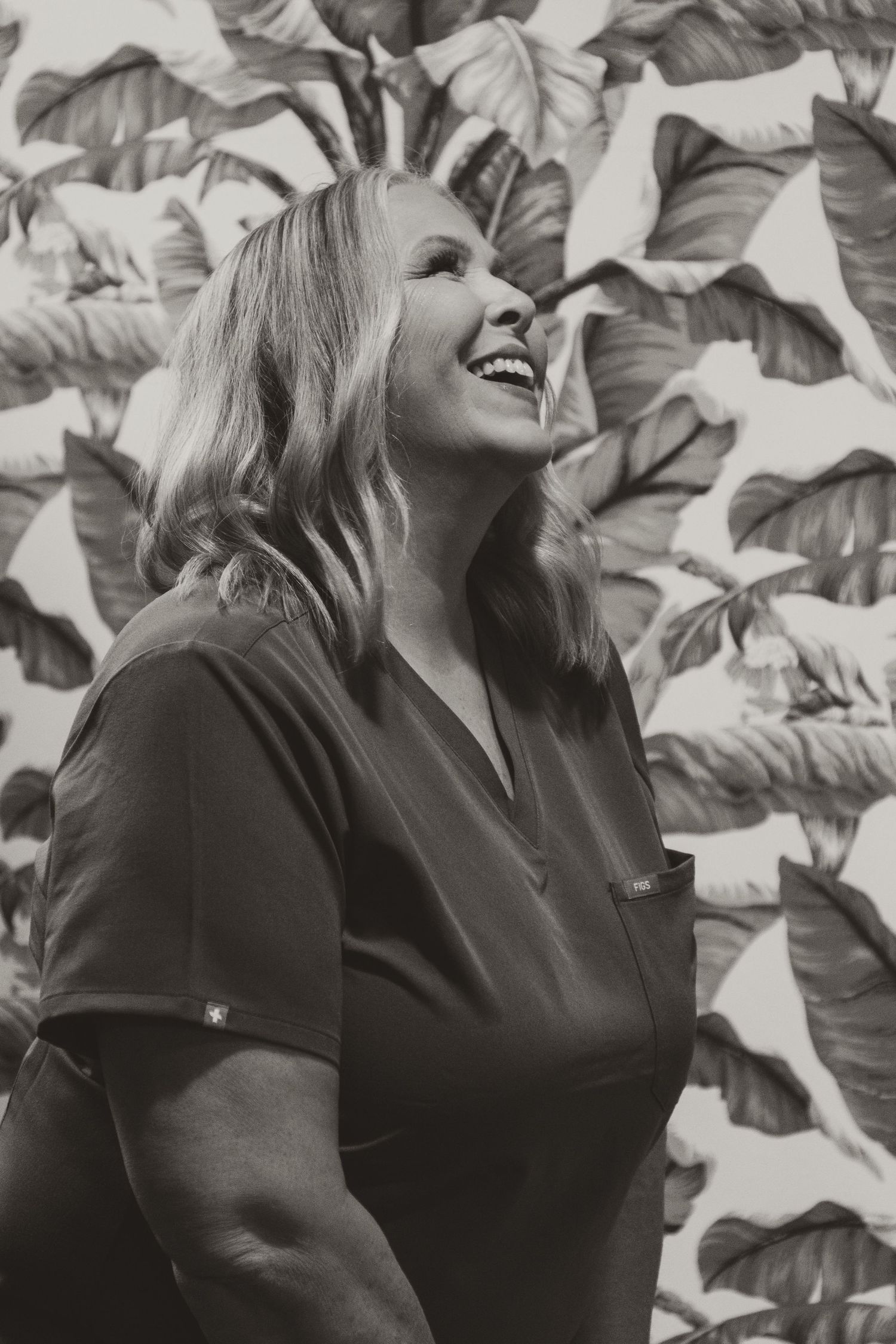 Black and white portrait of person laughing joyfully against a tropical leaf backdrop.