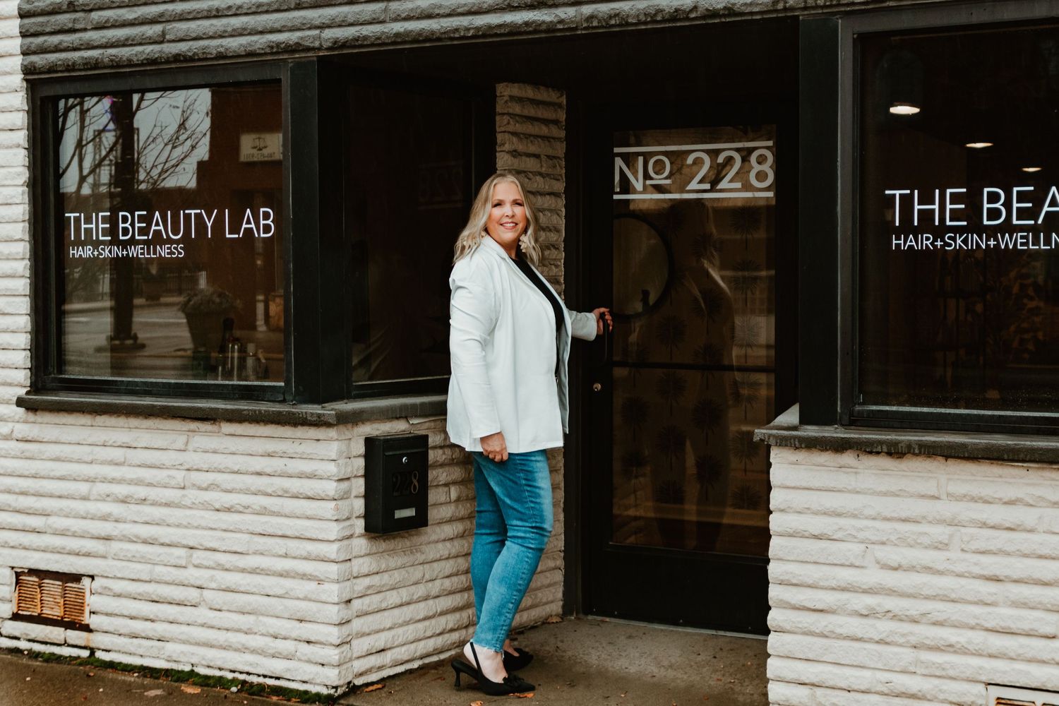 Beauty professional stands at entrance of The Beauty Lab salon storefront.