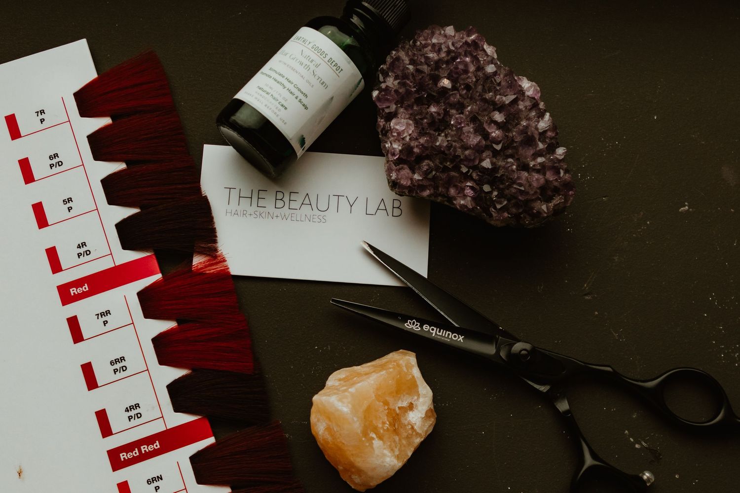 Hair color swatches with crystals and scissors on dark surface.