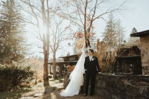 Wedding couple poses in front of rustic venue with sunlight streaming through winter trees. Wedding photographer Johnstown Somerset PA