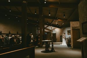 A dimly lit rustic wooden barn interior illuminated by soft natural light through windows creates a moody atmosphere.