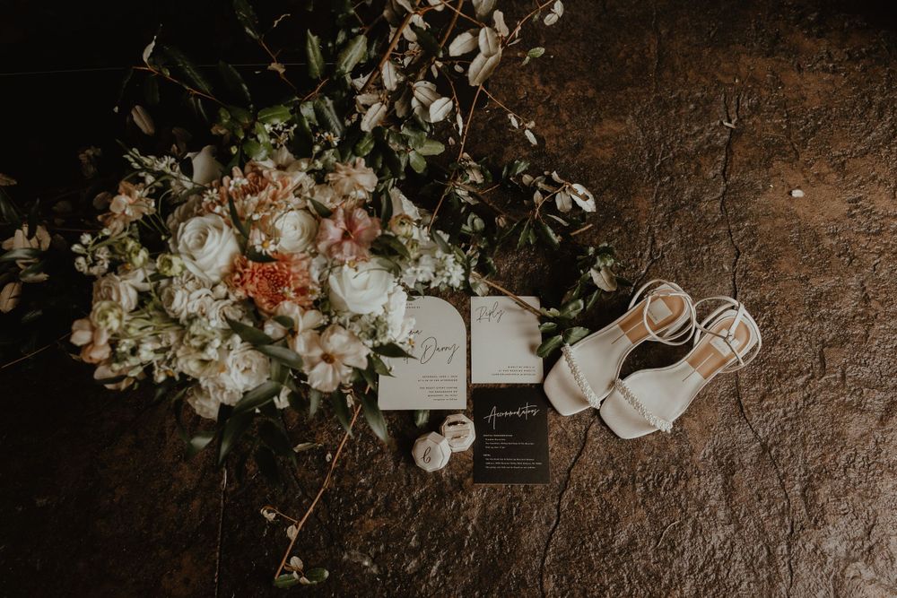 Wedding details including bridal shoes and floral arrangement on textured surface.