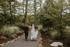 Couple walks down a garden path lined with ornamental grasses and pine trees. Wedding photographer Johnstown Somerset PA