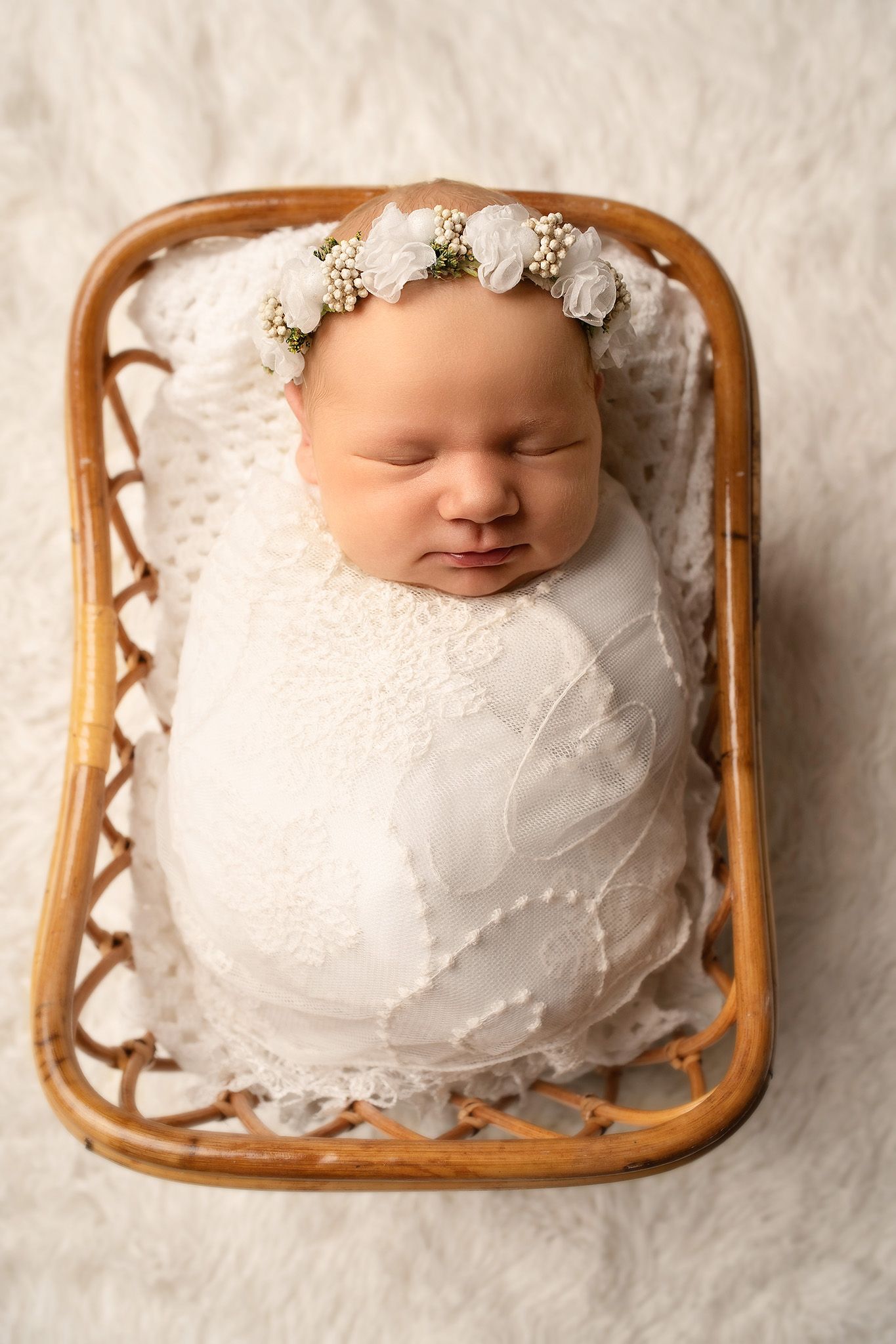 Newborn baby wrapped lace wrap in wooden basket on fluffy white rug