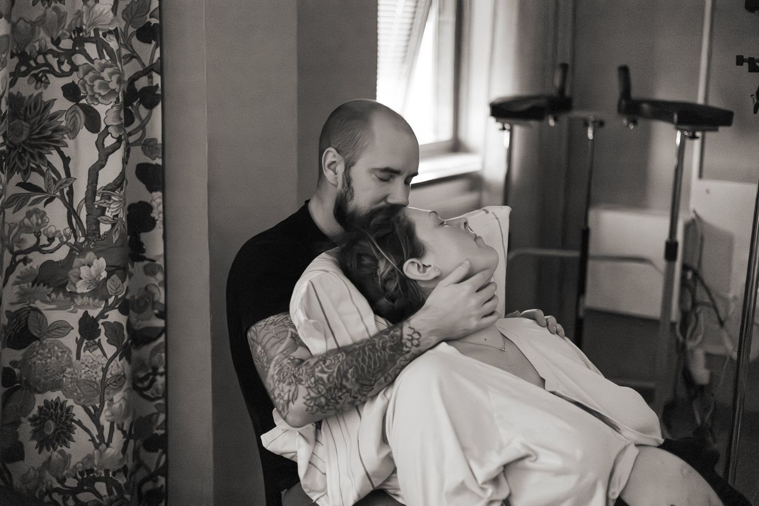 Förlossningsfoto i svartvitt på ett par där mannen sitter bakom kvinnan och stöttar henne