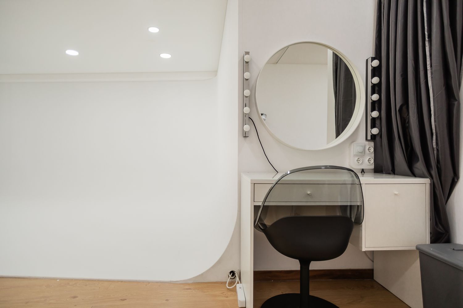 Minimalist makeup station with round illuminated mirror and black chair in white room.