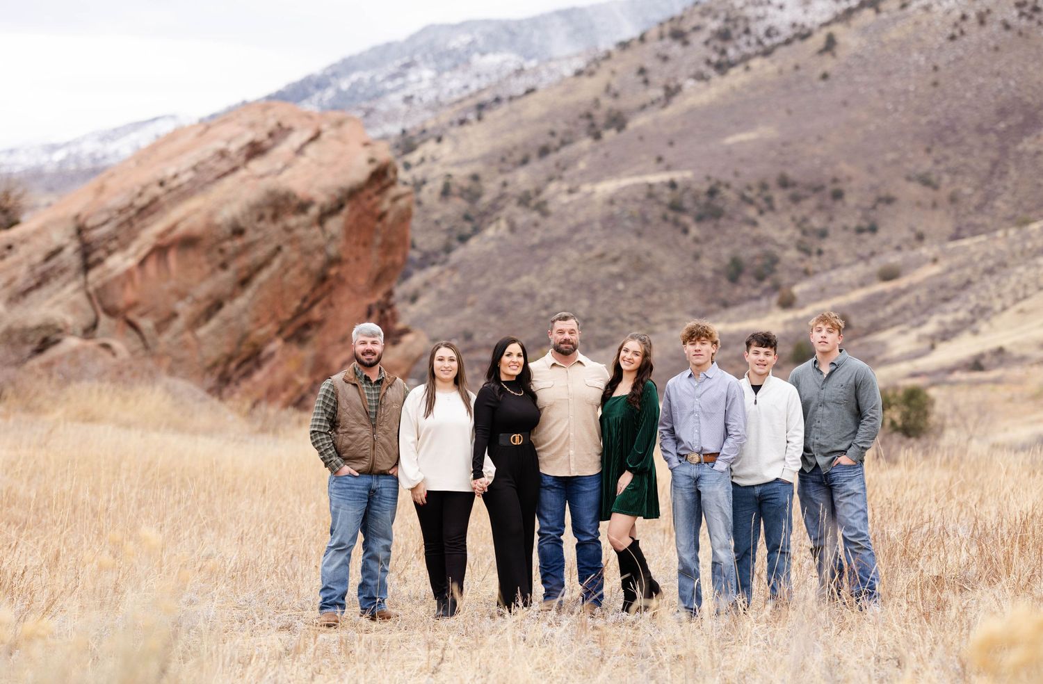 Extended family poses together on golden grass hill with mountains in background.