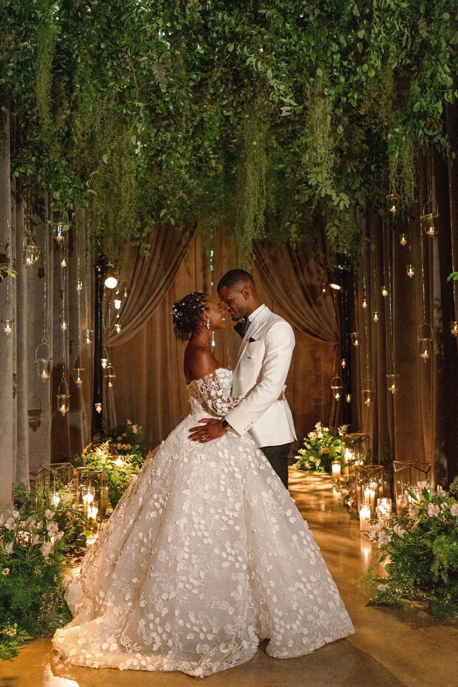 A romantic wedding portrait with hanging lights and greenery creating an enchanted forest backdrop.
