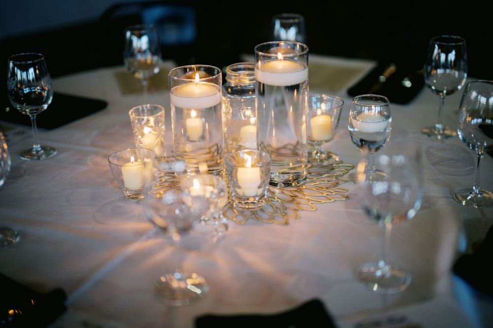 Elegant table setting with glowing candles in glass jars and wine glasses creating romantic ambient lighting.