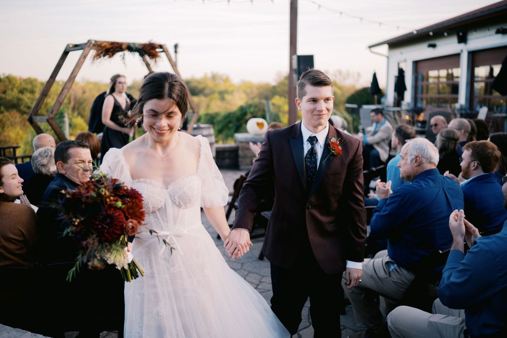 A couple celebrates at an outdoor wedding ceremony while guests watch from their seats at sunset.