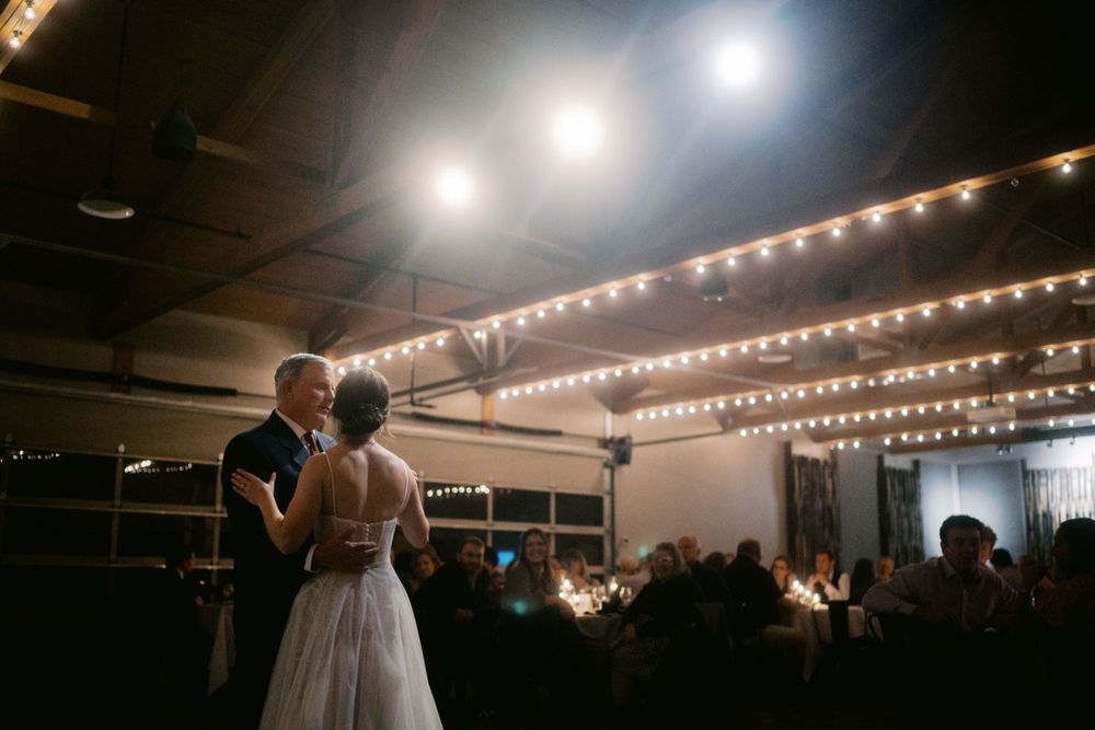 Happy couple dancing together under romantic string lights at their wedding reception in a dark venue.