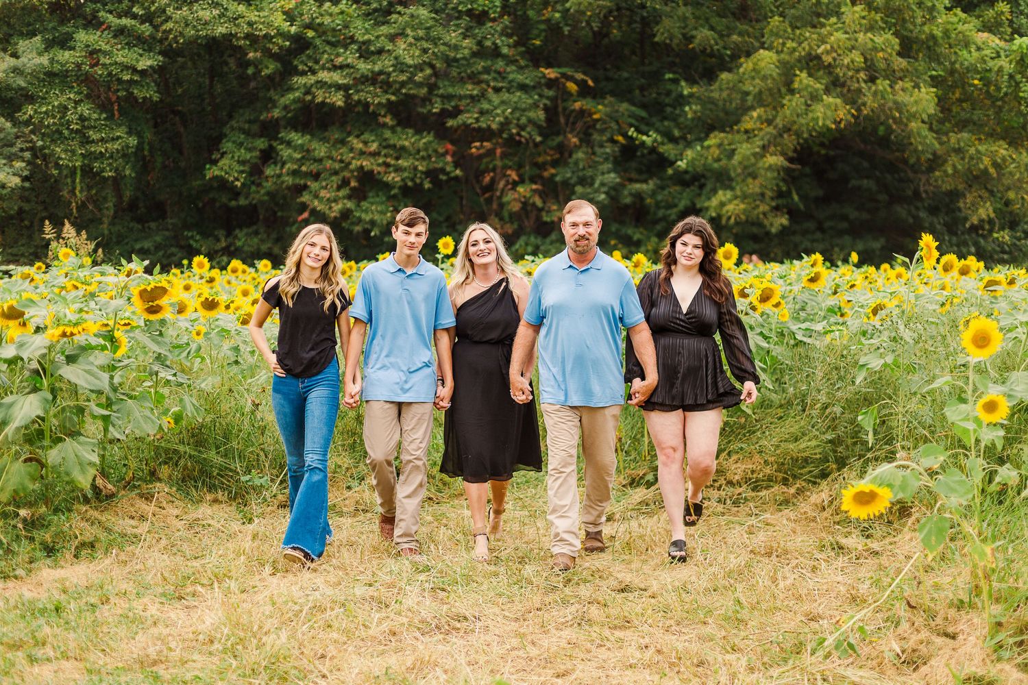 A group walking together through a sunny field of blooming sunflowers on a summer day.