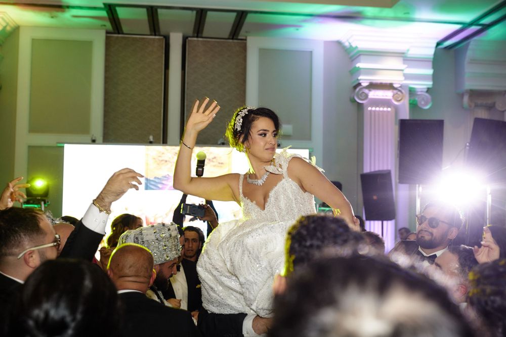 Person in white being lifted and celebrated by an energetic crowd at an event with green lighting.
