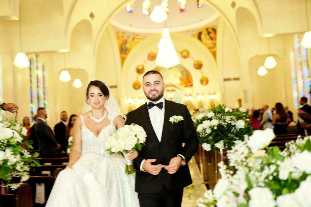 A wedding ceremony exit in an ornate church decorated with white floral arrangements and golden lighting.